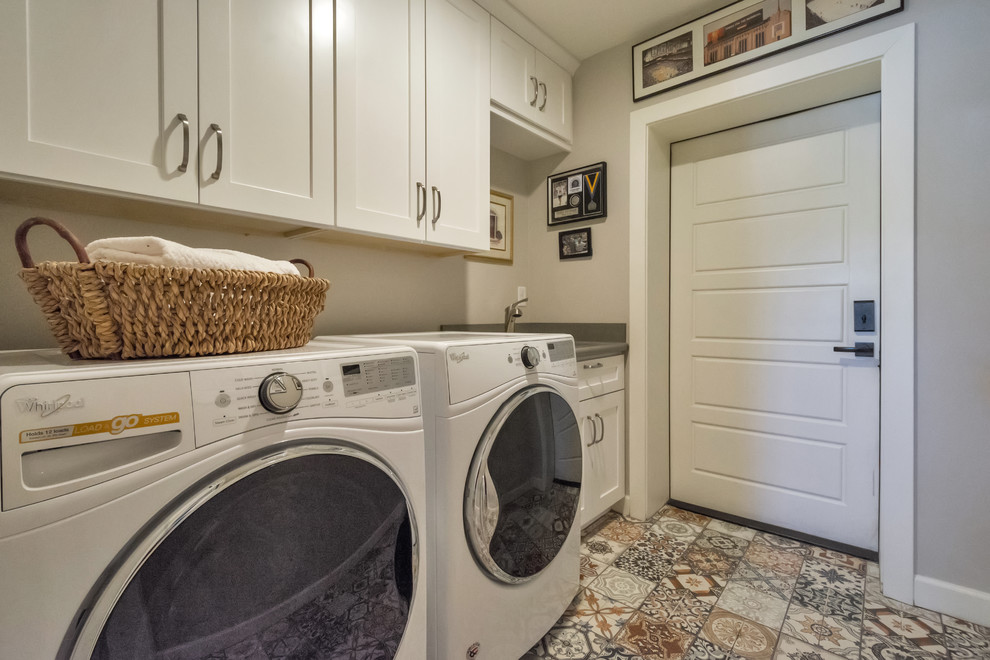 Photo of a small transitional single-wall dedicated laundry room in Phoenix with a drop-in sink, shaker cabinets, white cabinets, grey walls, porcelain floors, a side-by-side washer and dryer and multi-coloured floor.
