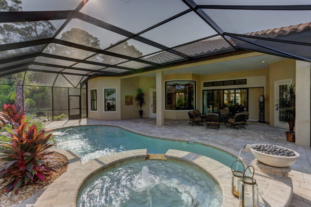This is an example of a large transitional backyard custom-shaped natural pool in Orlando with natural stone pavers and a hot tub.