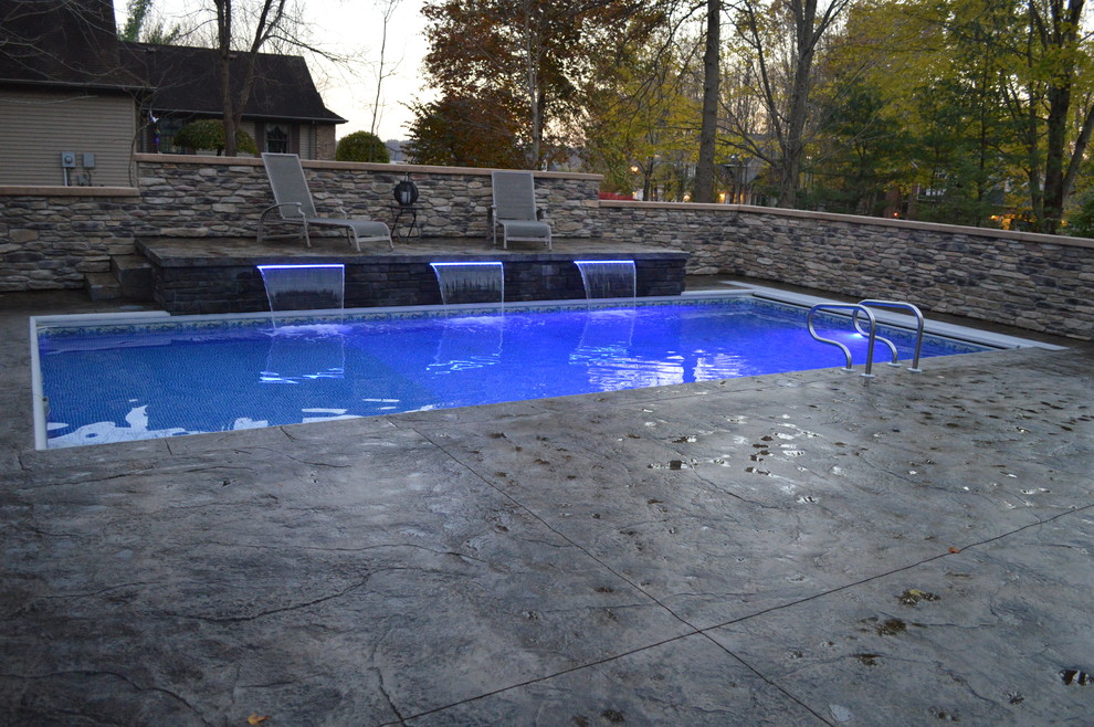 Traditional backyard rectangular pool in Columbus with a water feature and stamped concrete.