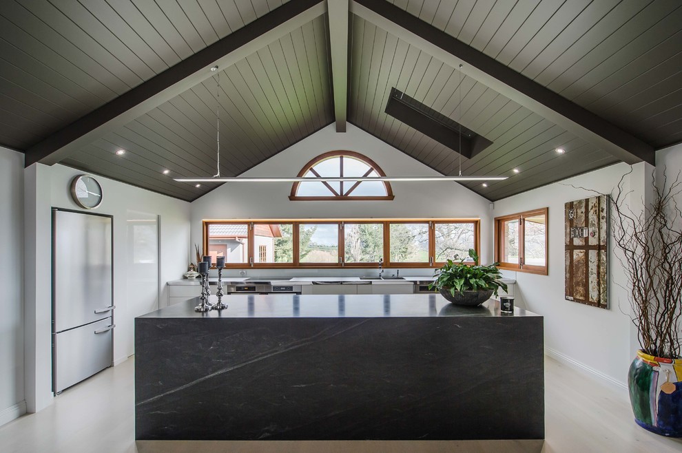 Photo of a mid-sized country u-shaped open plan kitchen in Hamilton with an integrated sink, white cabinets, stainless steel benchtops, white splashback, glass sheet splashback, light hardwood floors and with island.