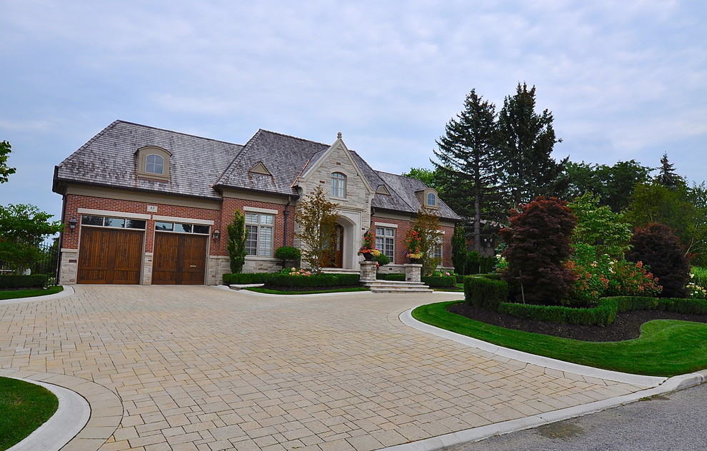 Photo of a large traditional front yard full sun driveway in Toronto with brick pavers and a garden path.