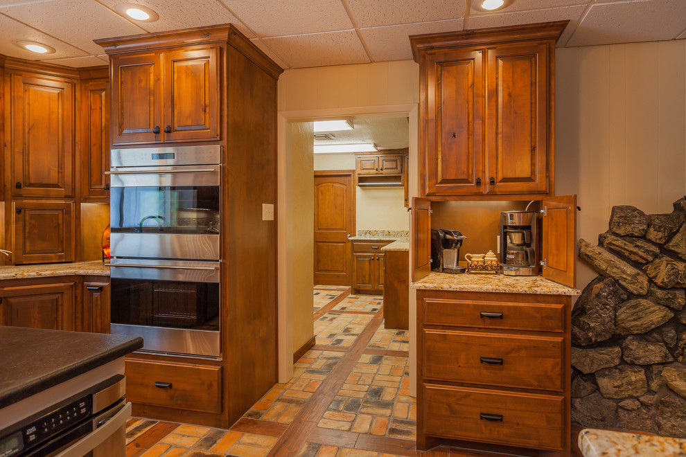 Inspiration for a large rustic l-shaped brick floor eat-in kitchen remodel in Dallas with a double-bowl sink, raised-panel cabinets, medium tone wood cabinets, granite countertops, beige backsplash, ceramic backsplash, stainless steel appliances and two islands