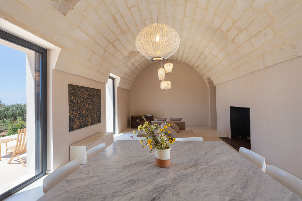 На фото: столовая в средиземноморском стиле с бежевыми стенами, стандартным камином, фасадом камина из металла, бежевым полом и сводчатым потолком
