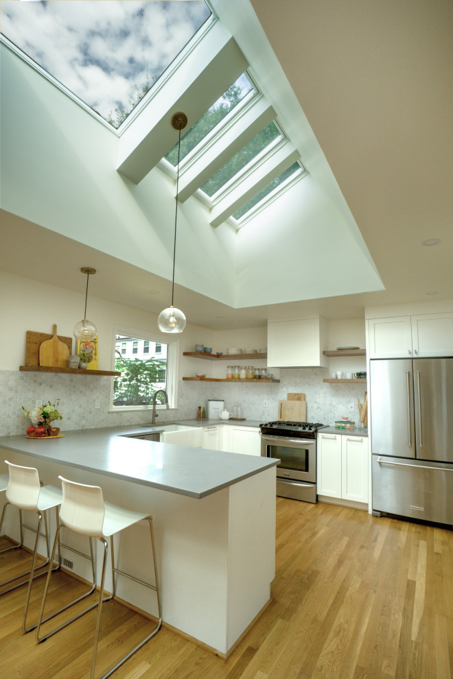 Mid-sized transitional u-shaped medium tone wood floor and vaulted ceiling eat-in kitchen photo with a farmhouse sink, shaker cabinets, white cabinets, quartz countertops, gray backsplash, marble backsplash, stainless steel appliances, a peninsula and gray countertops