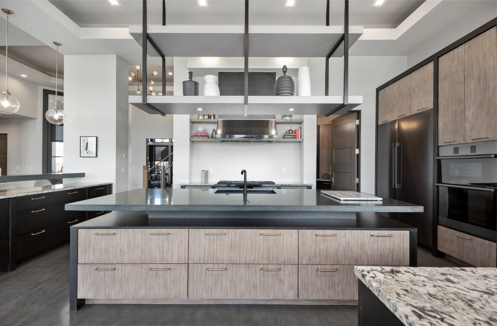 Photo of a large contemporary u-shaped kitchen pantry in Portland with a single-bowl sink, flat-panel cabinets, grey cabinets, limestone benchtops, white splashback, porcelain splashback, black appliances, concrete floors, multiple islands, grey floor, black benchtop and recessed.