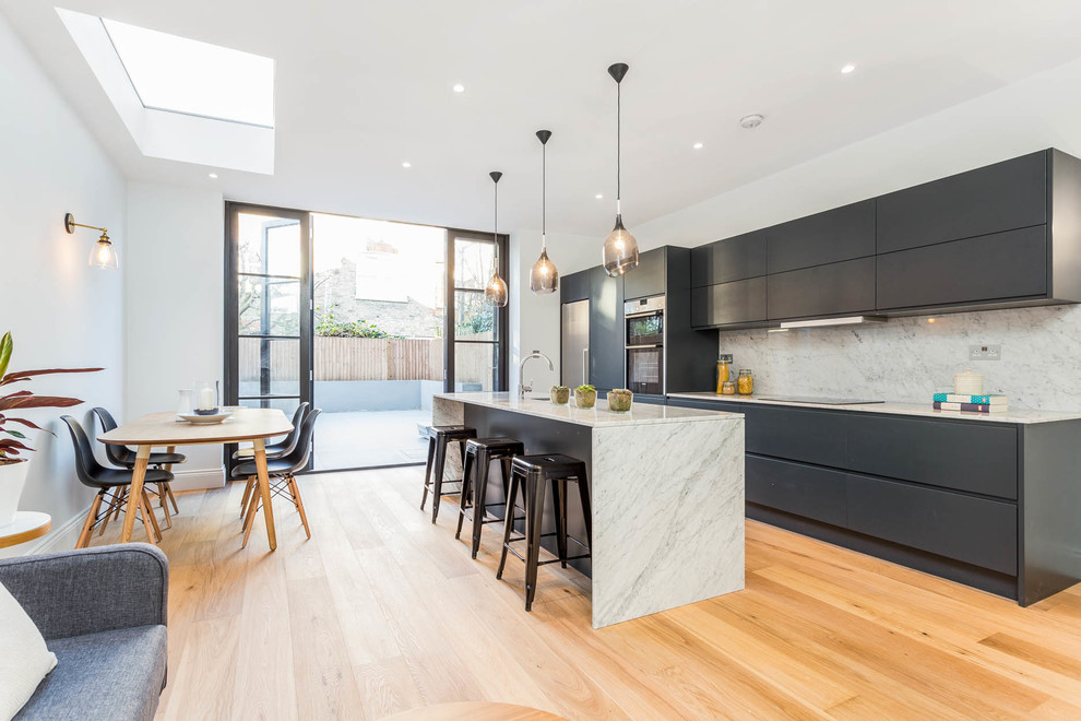Design ideas for a contemporary galley open plan kitchen in London with flat-panel cabinets, grey cabinets, white splashback, stainless steel appliances, medium hardwood floors, with island and brown floor.