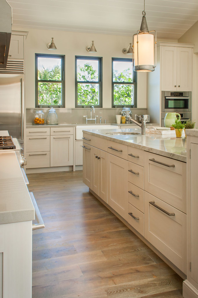 Photo of a large traditional l-shaped eat-in kitchen in San Diego with a farmhouse sink, recessed-panel cabinets, beige cabinets, quartzite benchtops, metallic splashback, metal splashback, stainless steel appliances and medium hardwood floors.