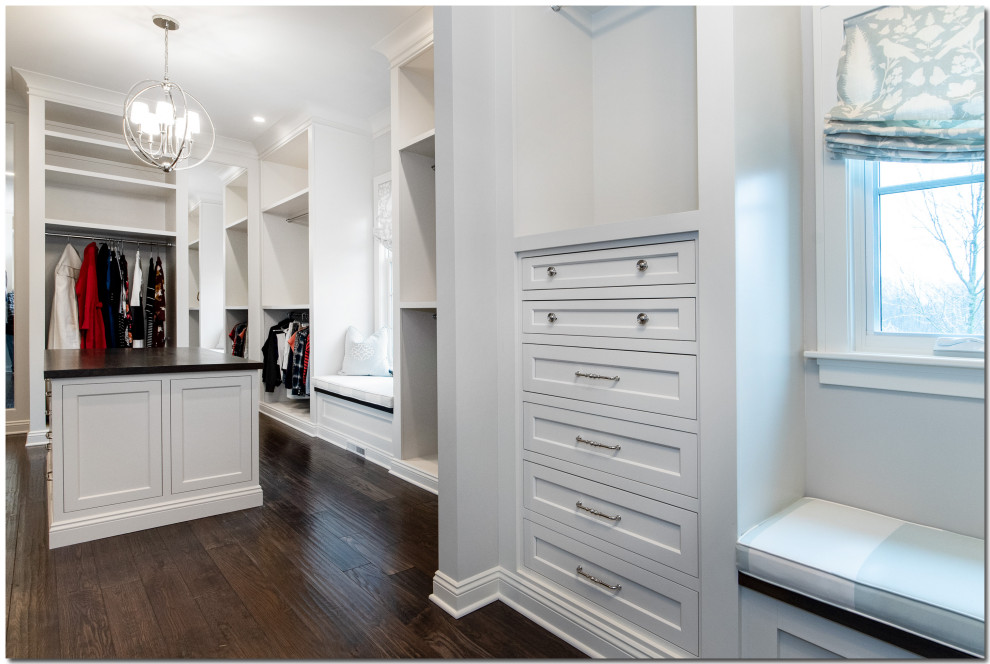 Photo of an expansive traditional gender-neutral dressing room in Cleveland with recessed-panel cabinets, white cabinets, dark hardwood floors and brown floor.