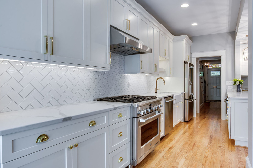 Inspiration for a mid-sized transitional galley light wood floor and beige floor eat-in kitchen remodel in DC Metro with a farmhouse sink, shaker cabinets, white cabinets, quartz countertops, white backsplash, subway tile backsplash, stainless steel appliances, a peninsula and white countertops