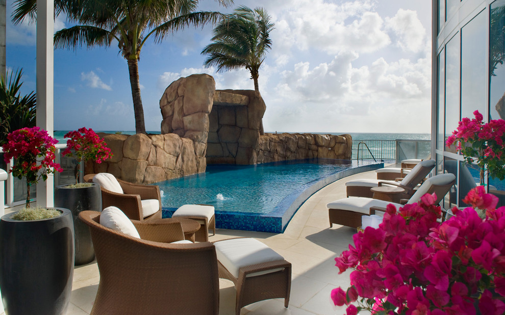 Design ideas for a large tropical backyard custom-shaped infinity pool in Miami with natural stone pavers.