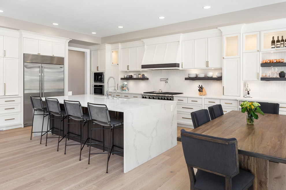 Transitional l-shaped eat-in kitchen in Portland with recessed-panel cabinets, white cabinets, white splashback, mosaic tile splashback, stainless steel appliances, light hardwood floors, with island, beige floor and white benchtop.