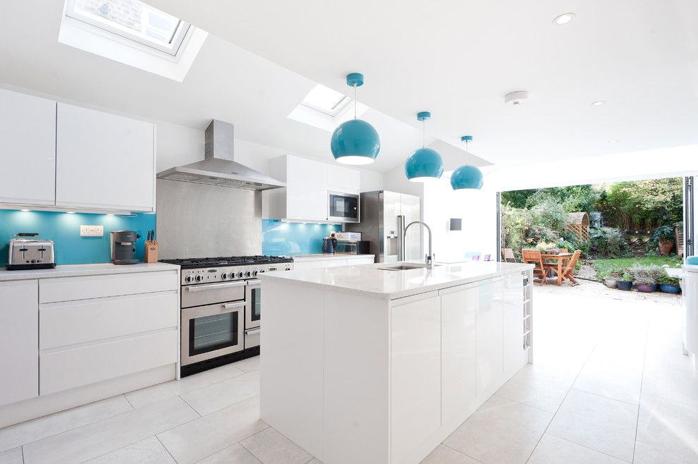 This is an example of a contemporary galley kitchen in London with flat-panel cabinets, white cabinets, blue splashback, stainless steel appliances and with island.