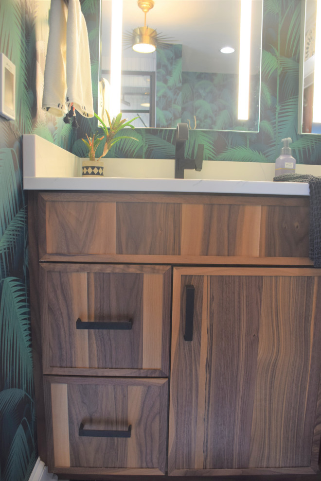 Идея дизайна: маленькая главная ванная комната со стиральной машиной в морском стиле с плоскими фасадами, фасадами цвета дерева среднего тона, ванной в нише, душем в нише, раздельным унитазом, белой плиткой, керамогранитной плиткой, зелеными стенами, полом из керамогранита, врезной раковиной, столешницей из искусственного кварца, черным полом, душем с раздвижными дверями, белой столешницей, тумбой под две раковины, встроенной тумбой и обоями на стенах для на участке и в саду