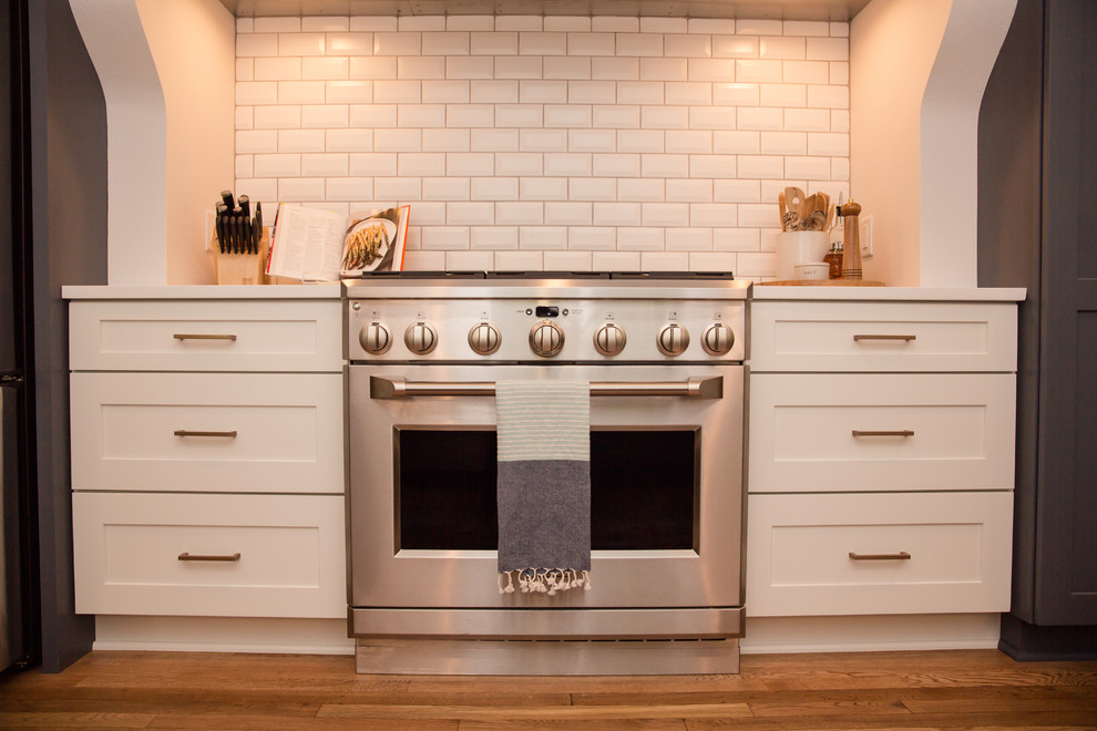 Mid-sized transitional galley medium tone wood floor and brown floor eat-in kitchen photo with an undermount sink, shaker cabinets, white cabinets, solid surface countertops, white backsplash, ceramic backsplash, stainless steel appliances, a peninsula and white countertops