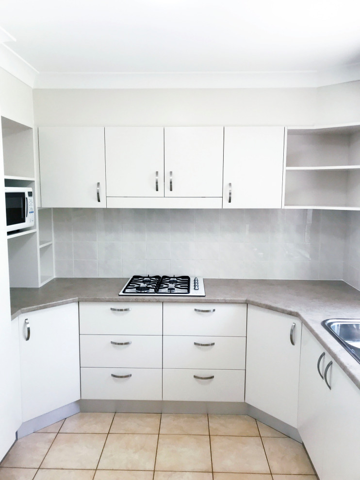 Inspiration for a mid-sized contemporary u-shaped kitchen pantry in Sydney with flat-panel cabinets, white cabinets, laminate benchtops, white splashback, glass sheet splashback, white appliances, no island and brown benchtop.