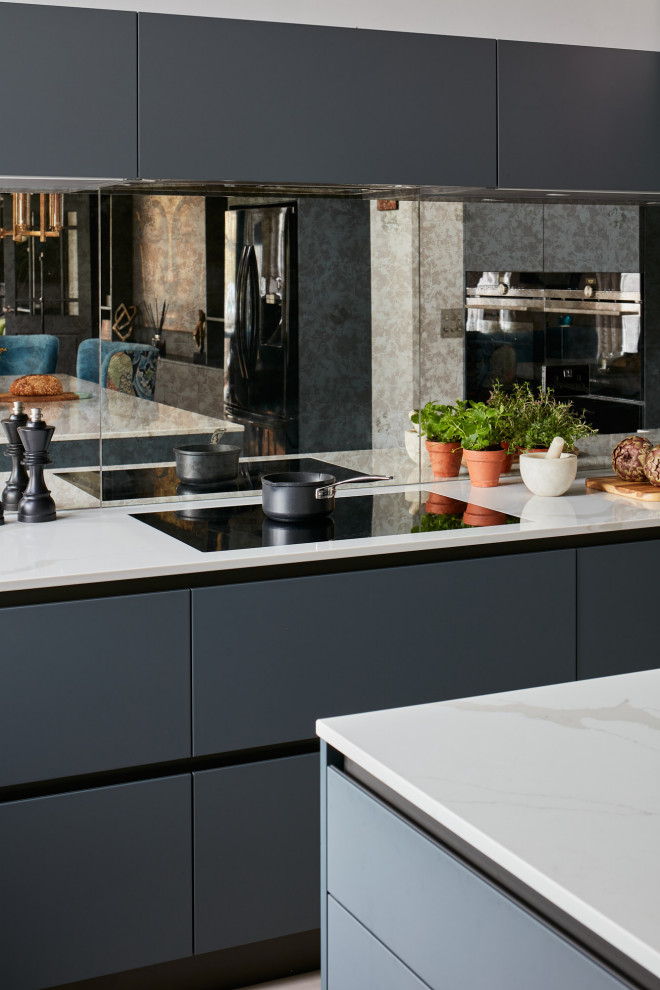 Photo of a medium sized modern u-shaped kitchen/diner in London with a built-in sink, flat-panel cabinets, grey cabinets, composite countertops, mirror splashback, black appliances, an island, white worktops and exposed beams.