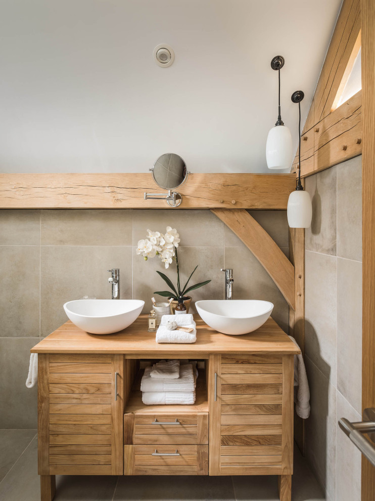 Aménagement d'une salle de bain campagne en bois clair avec un plan de toilette en bois, meuble double vasque, poutres apparentes et un placard à porte plane.