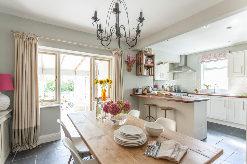 This is an example of a mid-sized transitional u-shaped eat-in kitchen in Other with shaker cabinets, white cabinets, grey splashback, subway tile splashback, a peninsula, grey floor, wood benchtops and slate floors.