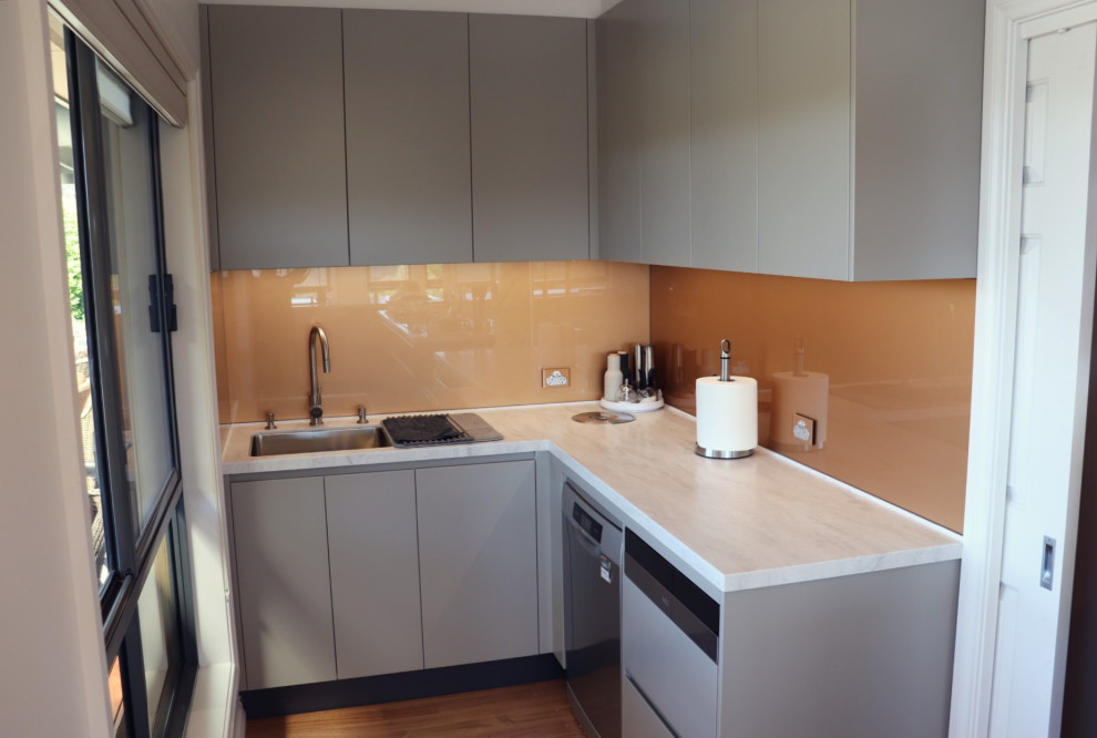 This is an example of a large modern l-shaped open plan kitchen in Canberra - Queanbeyan with a double-bowl sink, flat-panel cabinets, grey cabinets, solid surface benchtops, metallic splashback, glass sheet splashback, black appliances, medium hardwood floors, multiple islands, multi-coloured floor and multi-coloured benchtop.