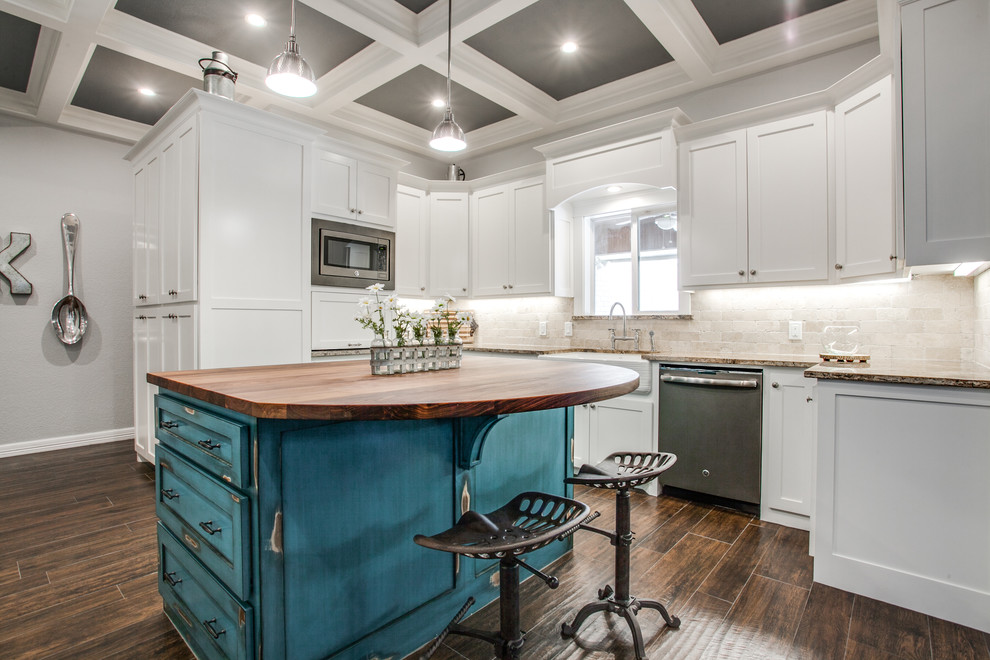 Photo of a mid-sized country u-shaped kitchen in Dallas with a farmhouse sink, shaker cabinets, white cabinets, granite benchtops, beige splashback, stone tile splashback, stainless steel appliances, medium hardwood floors, with island and brown floor.