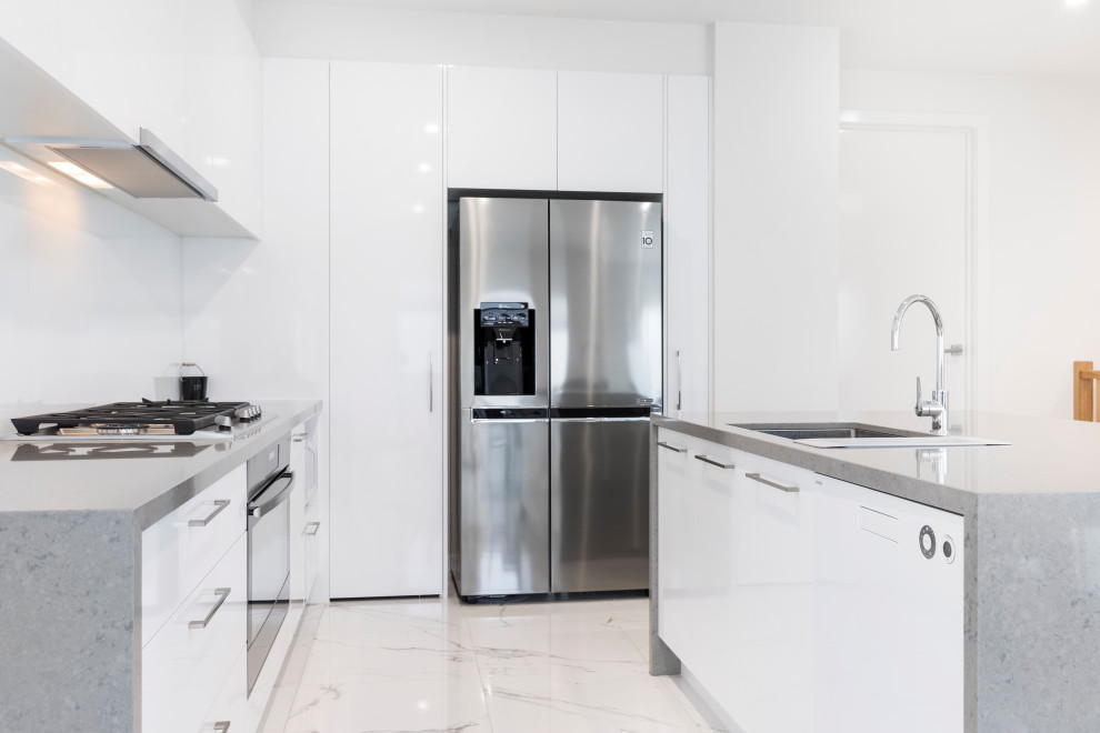 Photo of a mid-sized modern l-shaped kitchen pantry in Melbourne with an undermount sink, flat-panel cabinets, white cabinets, quartz benchtops, white splashback, glass sheet splashback, stainless steel appliances, porcelain floors, with island, white floor and grey benchtop.