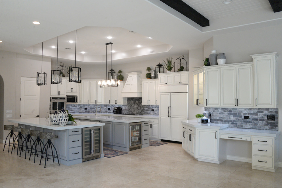 This is an example of a large modern eat-in kitchen in Phoenix with a farmhouse sink, raised-panel cabinets, white cabinets, quartz benchtops, grey splashback, brick splashback, stainless steel appliances, travertine floors, multiple islands, beige floor and white benchtop.