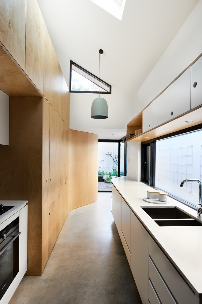 This is an example of a scandinavian kitchen in Sydney with a double-bowl sink, flat-panel cabinets, white cabinets, window splashback, concrete floors, no island, grey floor and white benchtop.
