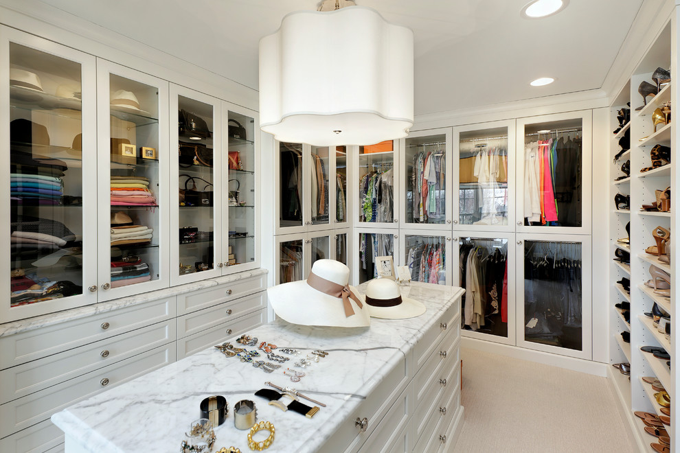 Design ideas for a large traditional gender-neutral walk-in wardrobe in Chicago with glass-front cabinets, white cabinets, carpet and beige floor.