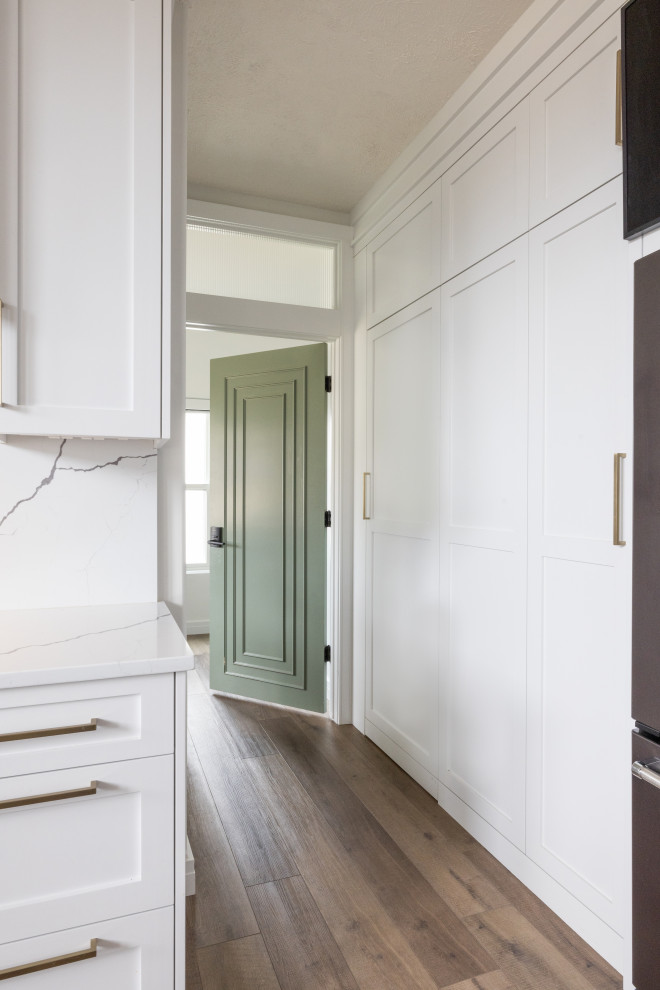 Inspiration for a mid-sized transitional vinyl floor and brown floor eat-in kitchen remodel in Omaha with an undermount sink, shaker cabinets, white cabinets, quartz countertops, white backsplash, stone slab backsplash, stainless steel appliances, an island and black countertops