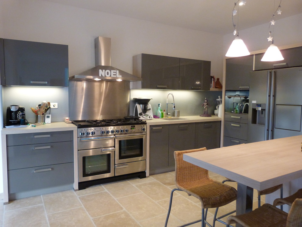 This is an example of a mid-sized contemporary single-wall open plan kitchen in Marseille with an integrated sink, grey cabinets, metallic splashback, metal splashback, stainless steel appliances and a peninsula.