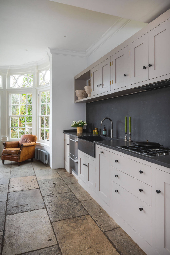 Inspiration for a large traditional open plan kitchen in London with shaker cabinets, quartzite benchtops, with island, a farmhouse sink, grey cabinets, black splashback, stone slab splashback, stainless steel appliances, brown floor and black benchtop.