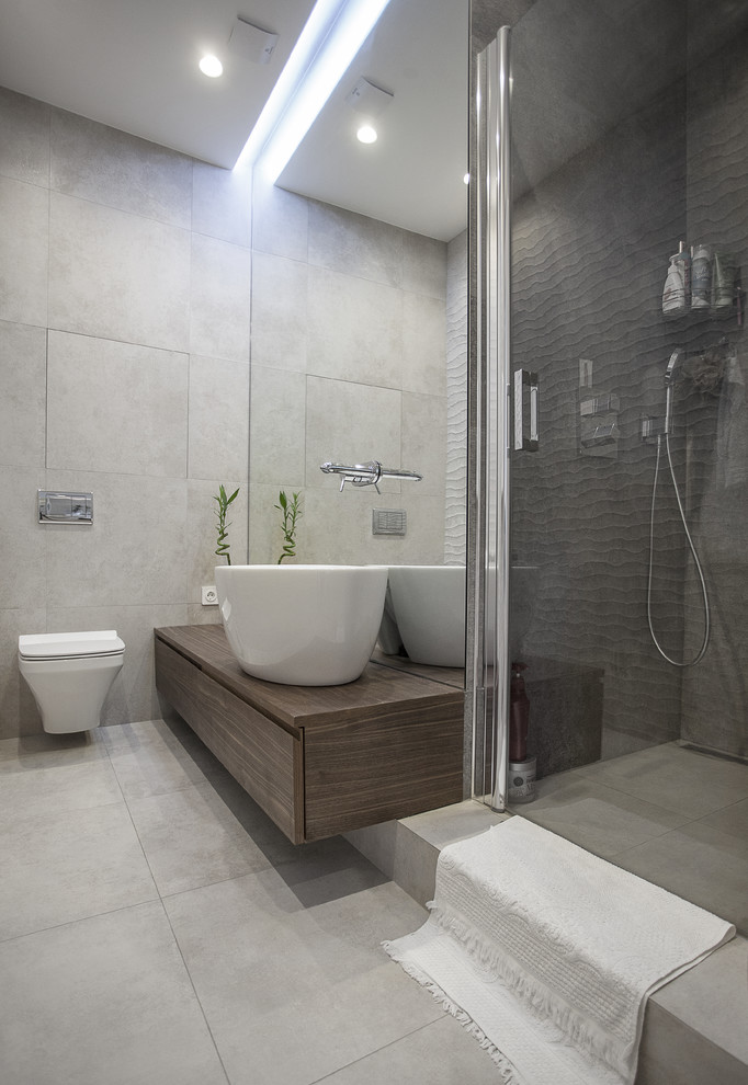 This is an example of a contemporary 3/4 bathroom in Moscow with flat-panel cabinets, dark wood cabinets, an alcove shower, a one-piece toilet, gray tile, white tile, a vessel sink, wood benchtops, grey floor, a hinged shower door and brown benchtops.