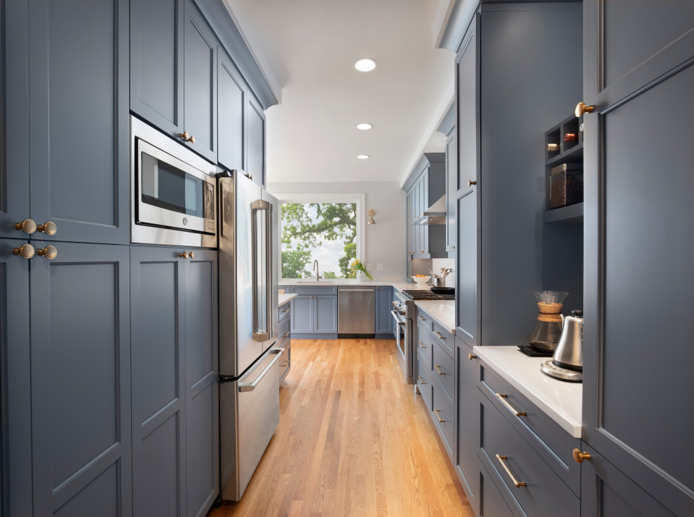 Photo of a traditional l-shaped kitchen/diner in DC Metro with a submerged sink, shaker cabinets, blue cabinets, engineered stone countertops, white splashback, stainless steel appliances, medium hardwood flooring, a breakfast bar, white worktops and porcelain splashback.