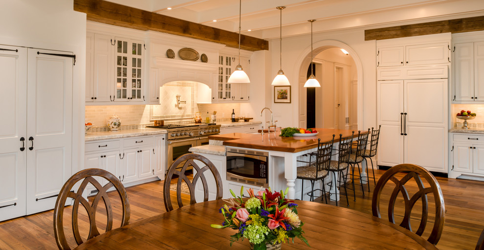 Design ideas for an expansive country l-shaped eat-in kitchen in Philadelphia with a farmhouse sink, raised-panel cabinets, white cabinets, marble benchtops, white splashback, stone tile splashback, stainless steel appliances, medium hardwood floors, with island and brown floor.