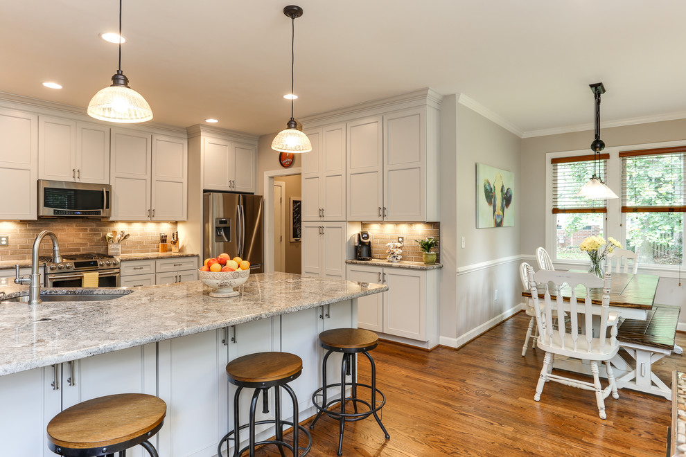 Photo of a large country u-shaped eat-in kitchen in Raleigh with an undermount sink, shaker cabinets, grey cabinets, granite benchtops, grey splashback, ceramic splashback, stainless steel appliances, medium hardwood floors and brown floor.