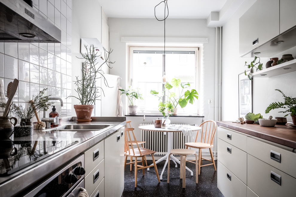 This is an example of a small scandinavian galley eat-in kitchen in Gothenburg with flat-panel cabinets, grey cabinets, stainless steel benchtops, white splashback, linoleum floors, no island and black floor.