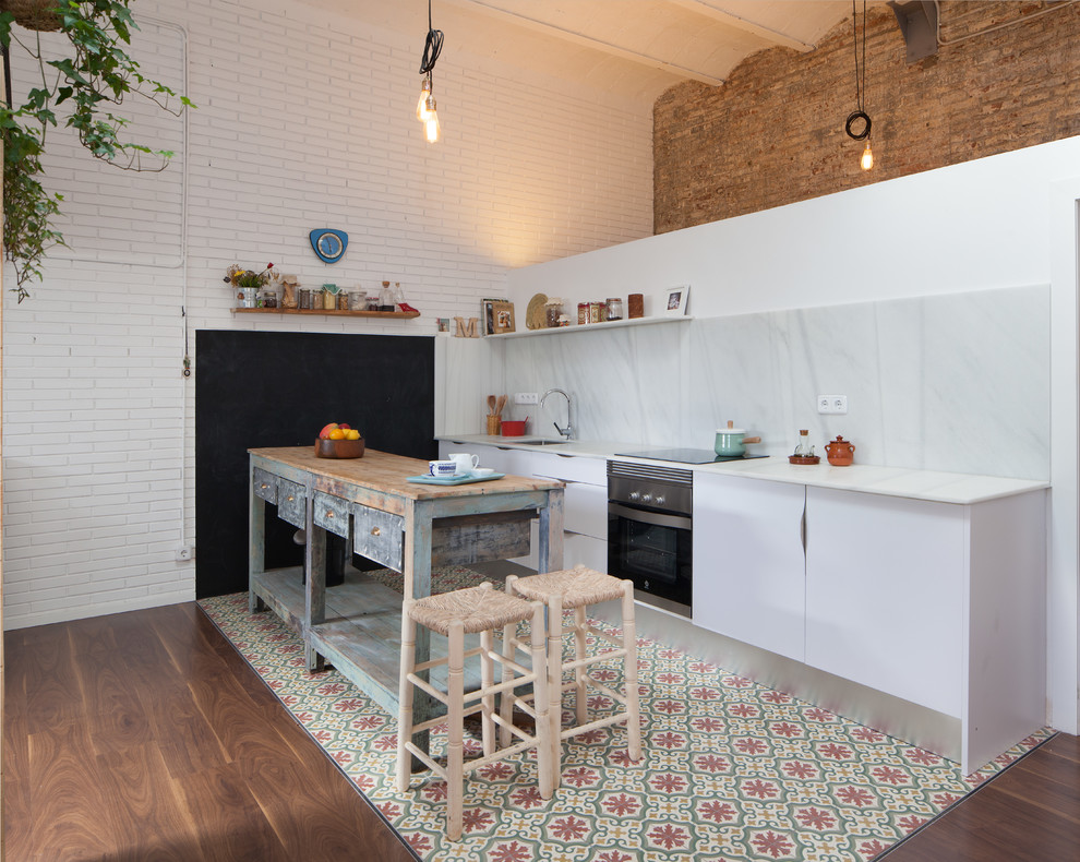 This is an example of a mid-sized mediterranean single-wall open plan kitchen in Barcelona with flat-panel cabinets, white cabinets, with island, an undermount sink, white splashback, stone slab splashback and black appliances.