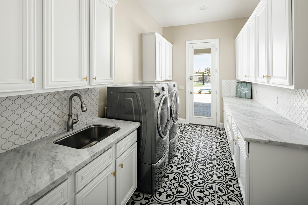 Design ideas for a mid-sized transitional galley dedicated laundry room in Phoenix with an undermount sink, white cabinets, quartz benchtops, beige walls, ceramic floors, a side-by-side washer and dryer, black floor, grey benchtop and recessed-panel cabinets.