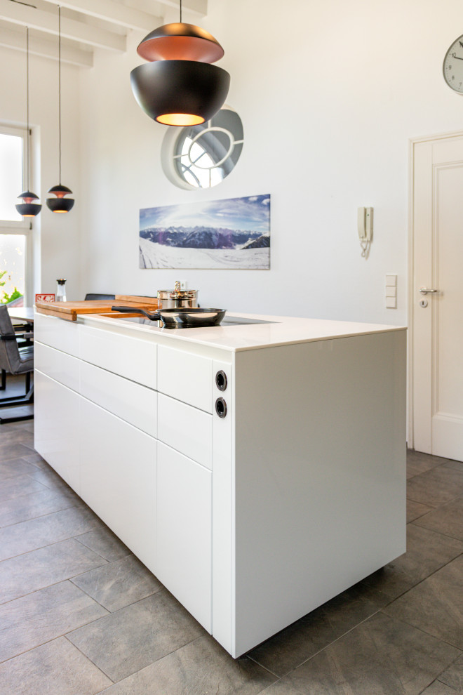 This is an example of a large modern galley eat-in kitchen in Stuttgart with an integrated sink, flat-panel cabinets, white cabinets, solid surface benchtops, black appliances, ceramic floors, with island, grey floor, white benchtop and exposed beam.
