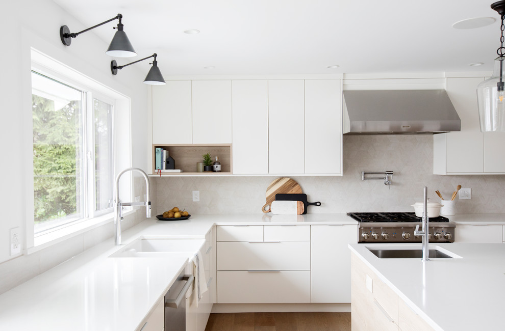 Photo of a mid-sized contemporary l-shaped kitchen in Vancouver with a farmhouse sink, flat-panel cabinets, white cabinets, stainless steel appliances, medium hardwood floors, with island, brown floor and grey benchtop.