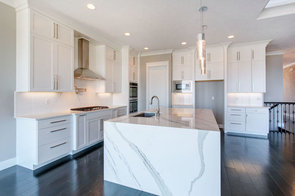 Photo of a large modern l-shaped open plan kitchen in Seattle with an undermount sink, shaker cabinets, white cabinets, quartz benchtops, white splashback, porcelain splashback, stainless steel appliances, dark hardwood floors, with island and white benchtop.