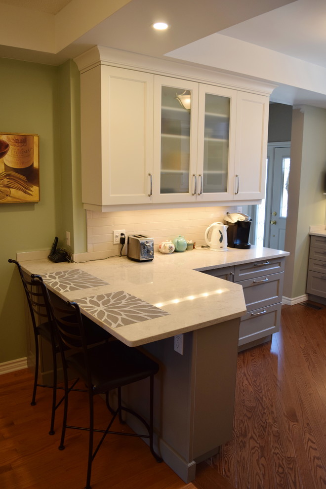 Mid-sized transitional l-shaped medium tone wood floor eat-in kitchen photo in Toronto with an undermount sink, shaker cabinets, white cabinets, quartz countertops, white backsplash, subway tile backsplash, stainless steel appliances and a peninsula