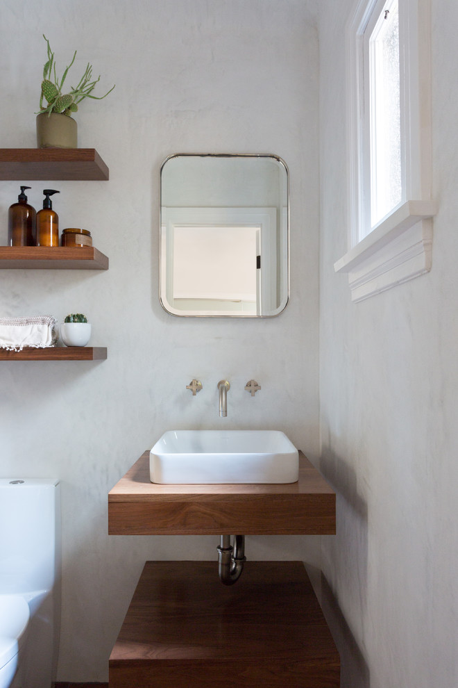 Photo of a small mediterranean powder room in Los Angeles with open cabinets, a vessel sink, wood benchtops and beige walls.