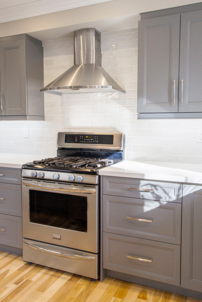 Example of a transitional brown floor kitchen design with gray cabinets, quartz countertops, gray backsplash, ceramic backsplash, stainless steel appliances and white countertops