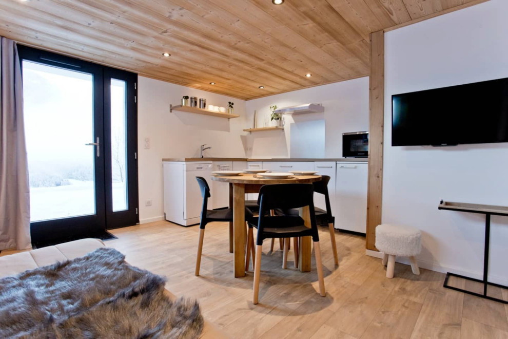 Imagen de sala de estar abierta nórdica grande sin chimenea con paredes blancas, suelo laminado, televisor colgado en la pared y madera