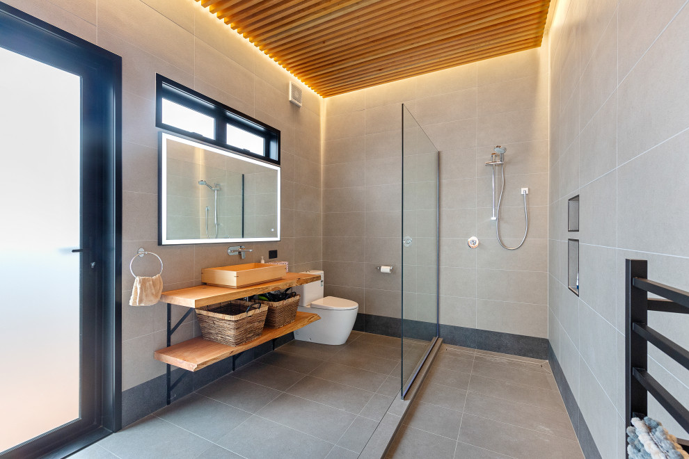 Design ideas for an asian bathroom in Auckland with open cabinets, light wood cabinets, an open shower, gray tile, grey walls, a vessel sink, wood benchtops, grey floor, an open shower, a niche, a single vanity, a built-in vanity, wood and wood walls.