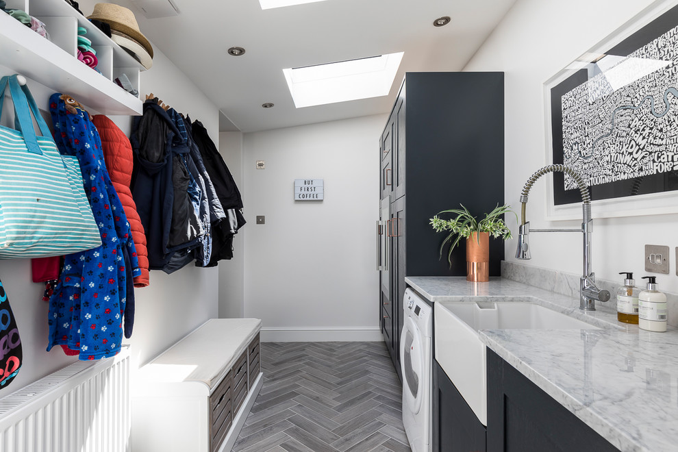 Photo of a mid-sized contemporary dedicated laundry room in London with a farmhouse sink, recessed-panel cabinets, marble benchtops, grey floor and black cabinets.
