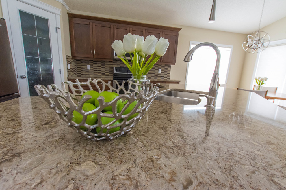 Eat-in kitchen - mid-sized transitional l-shaped ceramic tile and beige floor eat-in kitchen idea in Edmonton with a double-bowl sink, shaker cabinets, brown cabinets, quartz countertops, beige backsplash, glass tile backsplash, stainless steel appliances and an island