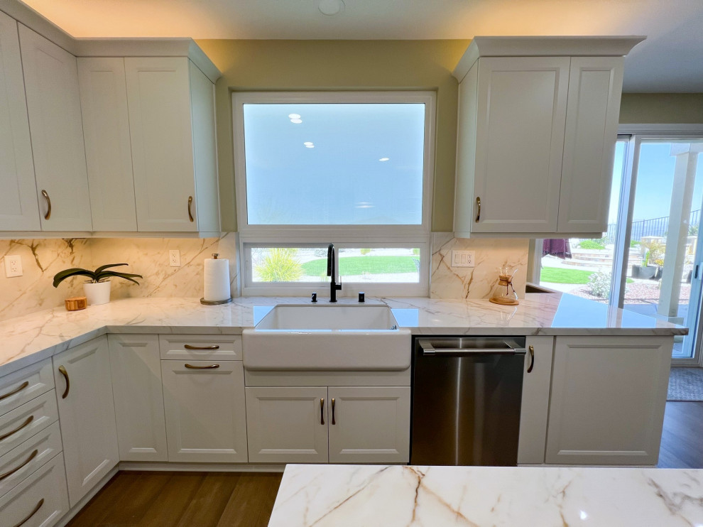 Large contemporary l-shaped eat-in kitchen in San Diego with a farmhouse sink, shaker cabinets, white cabinets, quartz benchtops, white splashback, engineered quartz splashback, stainless steel appliances, vinyl floors, with island, brown floor and white benchtop.