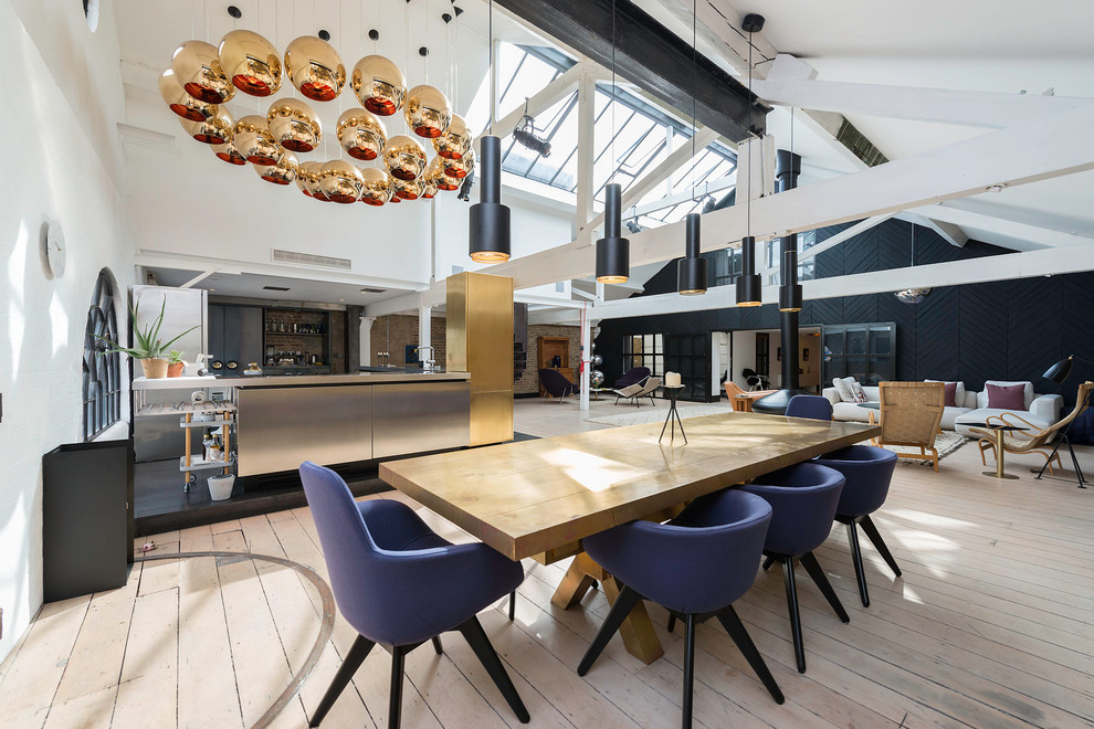 Photo of a large industrial open plan dining in London with white walls, light hardwood floors, a hanging fireplace and a metal fireplace surround.